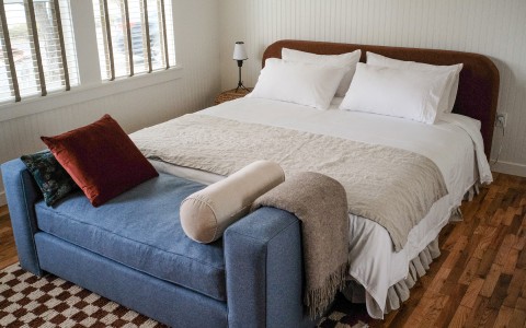 A large bed with white and khaki colored sheets and the sun shining in from the windows.