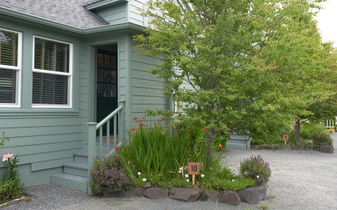 A small walkway with flowers and plants and a sign with the number ten on it leading to a light green house.