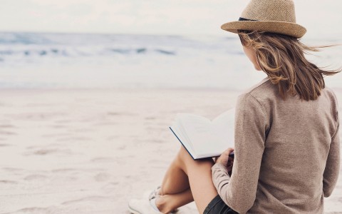 A lady sitting on a beach reading a book.