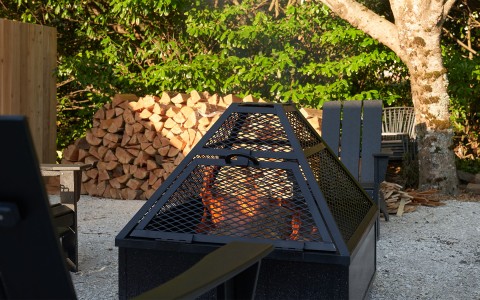 A black lit fire pit with logs stacked behind it and the sun setting.