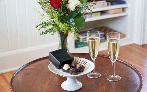 A small white platter with assorted chocolates on top and two glasses of champagne to the right.