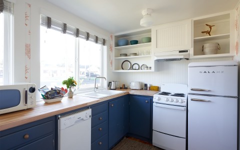 A kitchen with white appliances and navy colored cabinets.