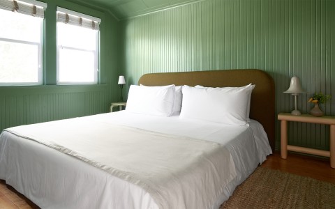 A large bed with an olive colored headboard and a small wooden table on each side.