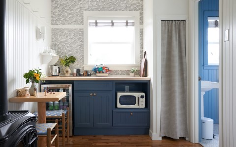 A small kitchen with blue colored cabinets and a bathroom to the right.