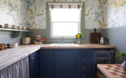 A small kitchen with blue cabinets and green and white design wallpaper.