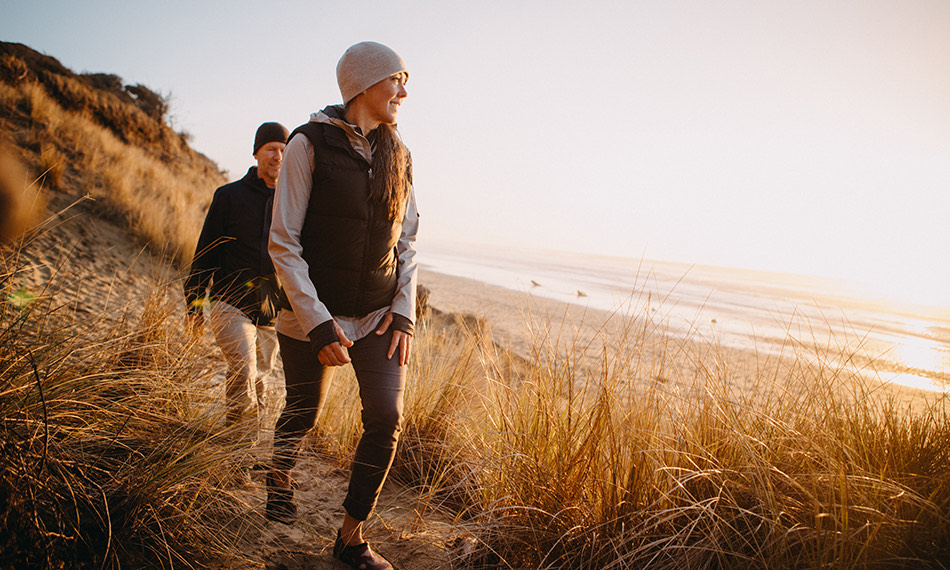 A couple walking near the ocean in a grassy area as the sun is setting.