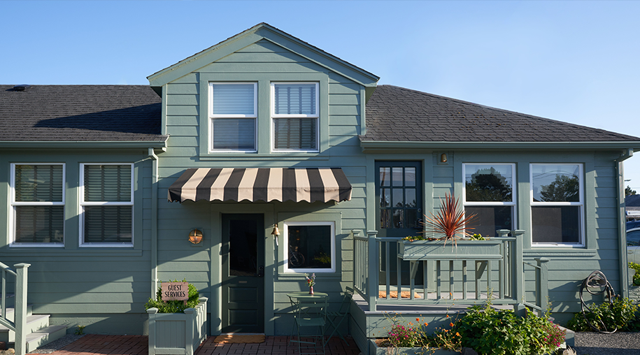 A light green colored cottage with flowers next to the entrances.