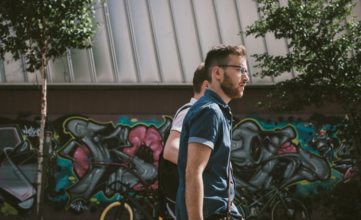 two guys walking together outside by a wall with graffiti