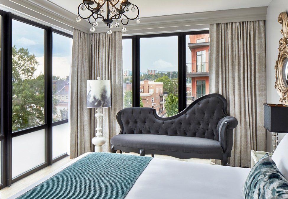 a guestroom with an asymmetric couch next to a lamp with a view of the bed and decorative gold mirror