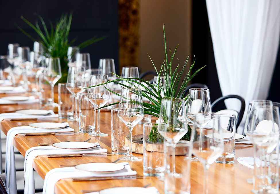 table settings at a long rectangular table and two plants as center pieces