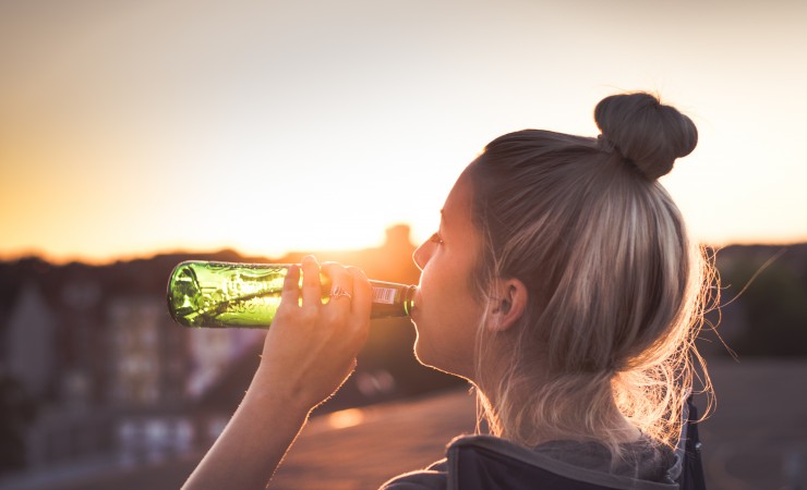 girl with her hair up drinking a beer with a sunset in the background