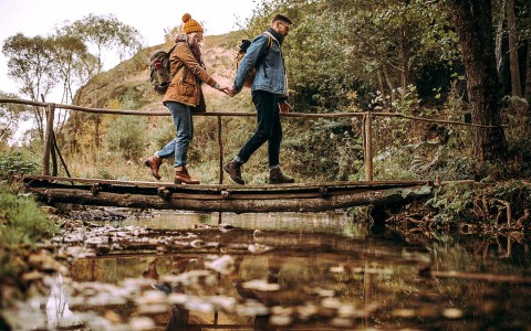 View of a couple crossing a wooden bridge in the middle of nature