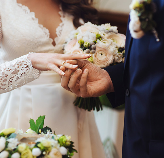 Close up of a groom putting the ring on the bride's finger