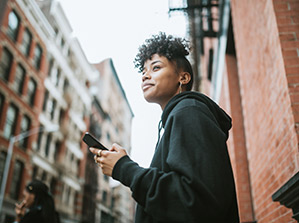 woman in the street holding her phone while she is looking to the left side