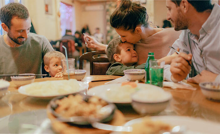 woman kissing her child while they eat dinner