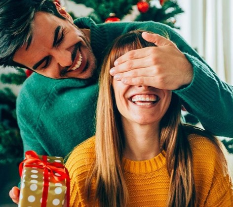 couple in a green and yellow sweater surprising each other with gifts