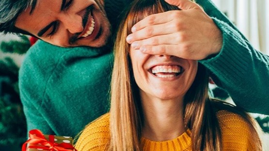 couple in a green and yellow sweater surprising each other with gifts
