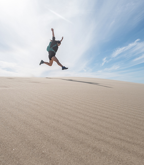woman jumping in a sand dune at noon