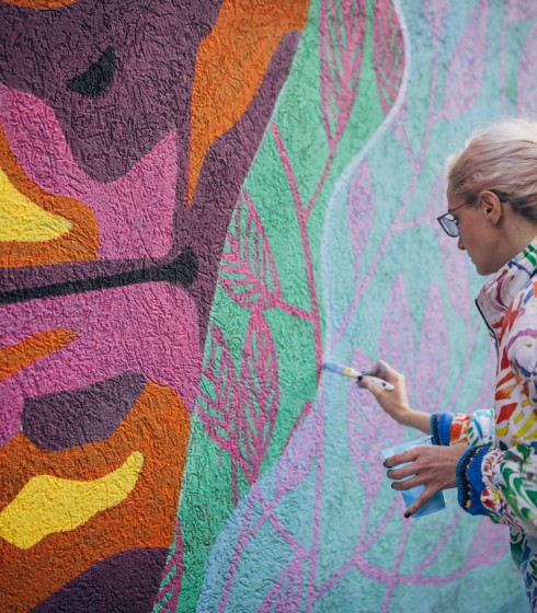 lady in colorful jacket painting a colorful wall
