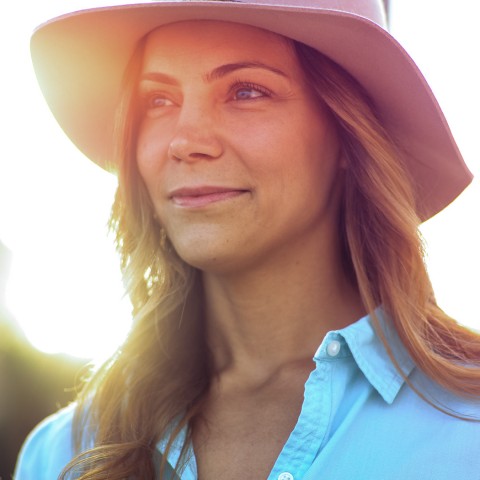 woman wearing a hat smiling outside with sun gleaming behind her