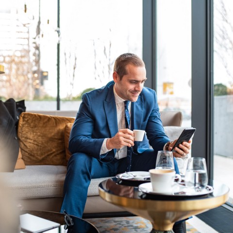 business man sitting on a couch looking at his phone smiling