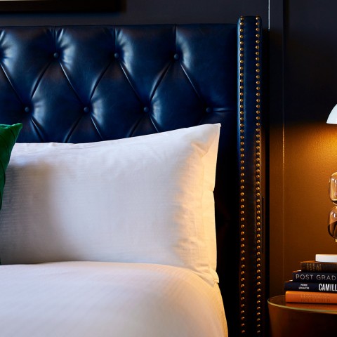 closeup of a bed with white sheets and a blue leather headboard