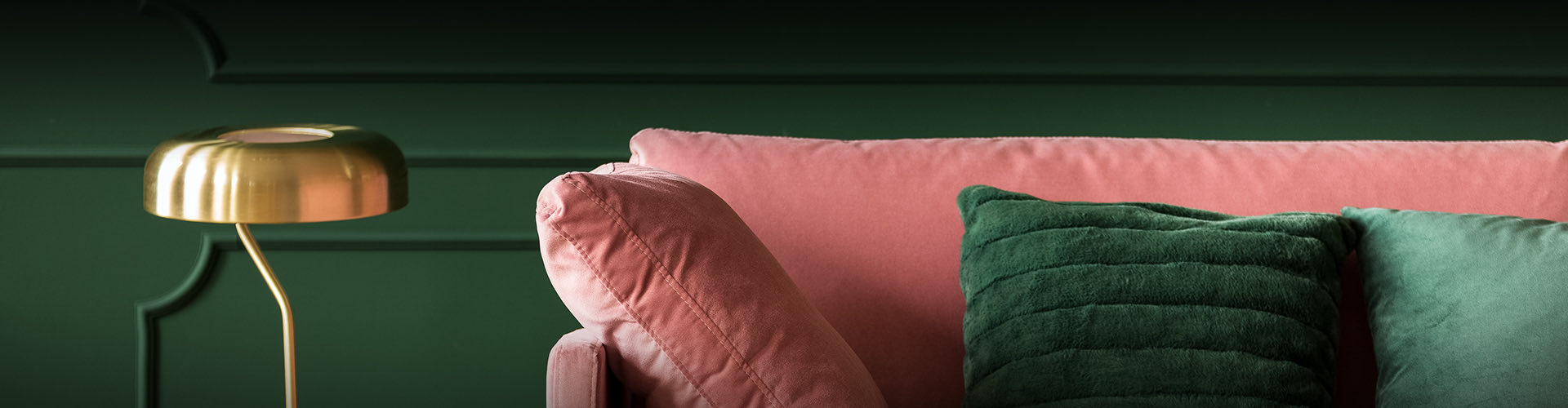 pink velvet couch with a green accent pillow in a dark green room