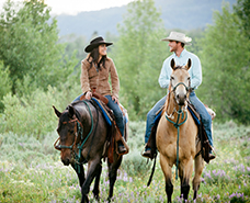 two people riding horses in the woods