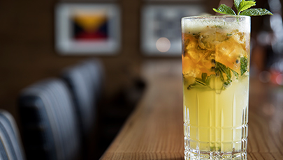 yellow cocktail sitting on bar with mint garish