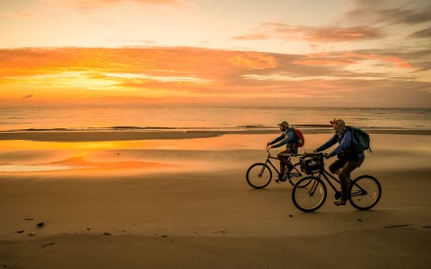 two people biking on the beach at sun set 