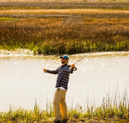 a man standing next to the water while fly fishing