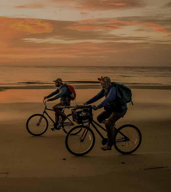 two people biking on the beach at sun set