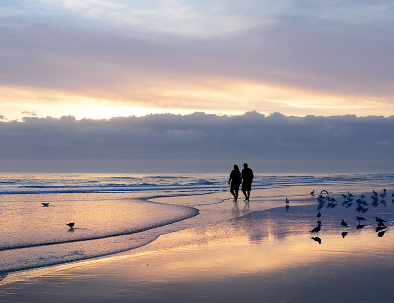two people walking on the beach during sun set 