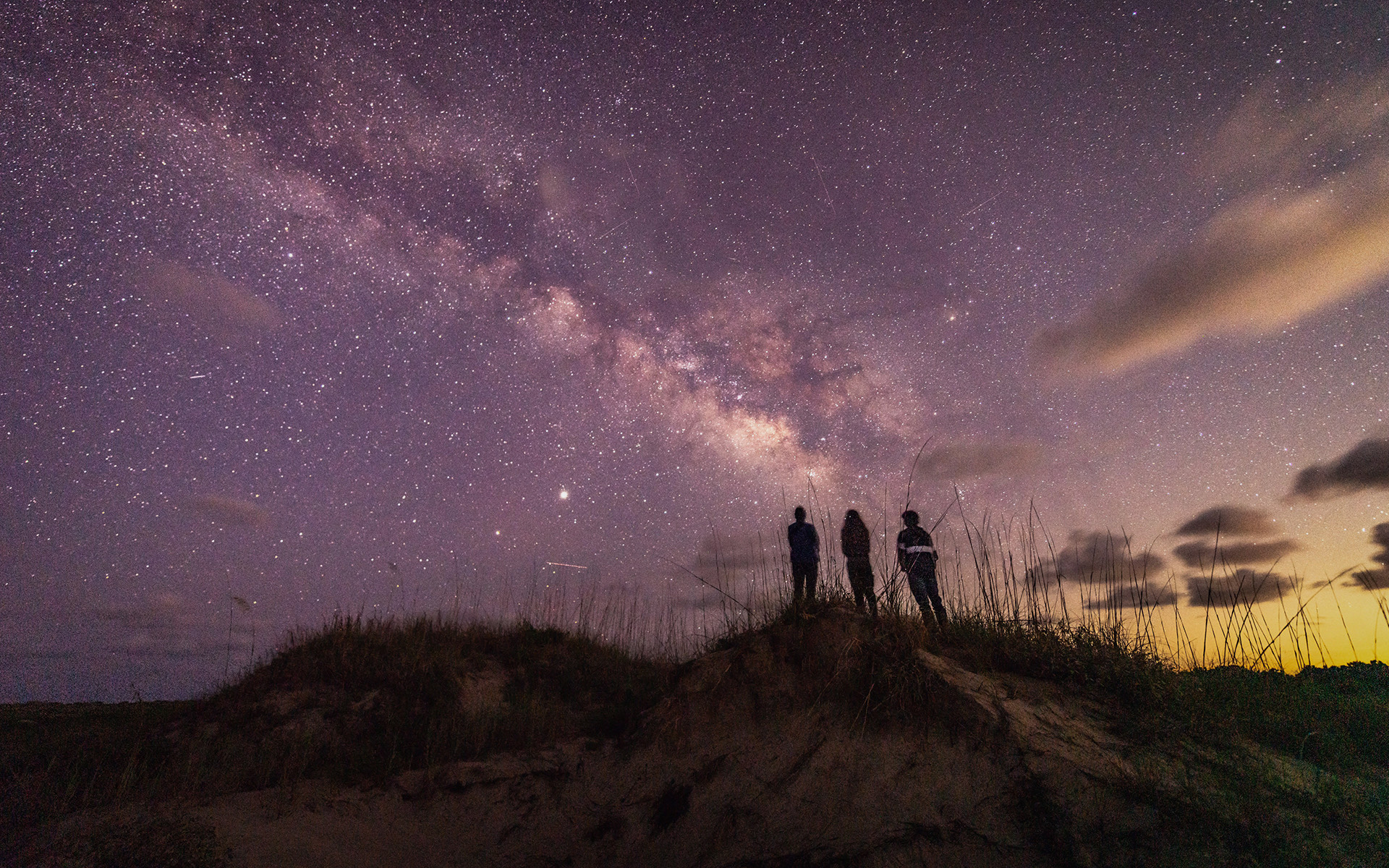 three people stargazing on a hill 