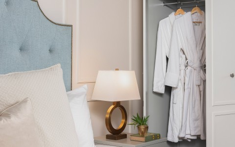  light blue headboard with modern lamp and two robes hanging in the closet 