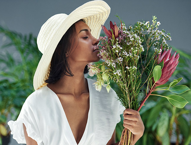 woman smelling flowers while wearing a white dress and a sun hat