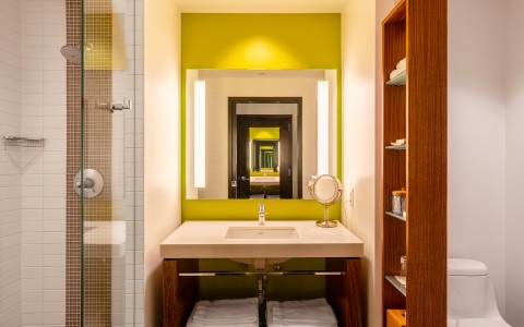 bathroom with a lime green wall behind the mirror and sink and a clear glass shower to the left