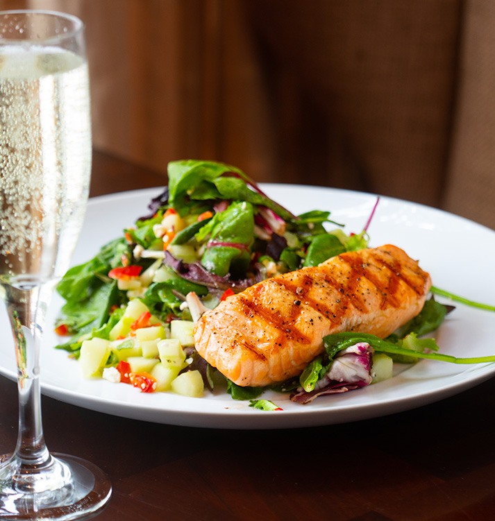 close up of a salmon dish with a salad and a bubbly drink on the side