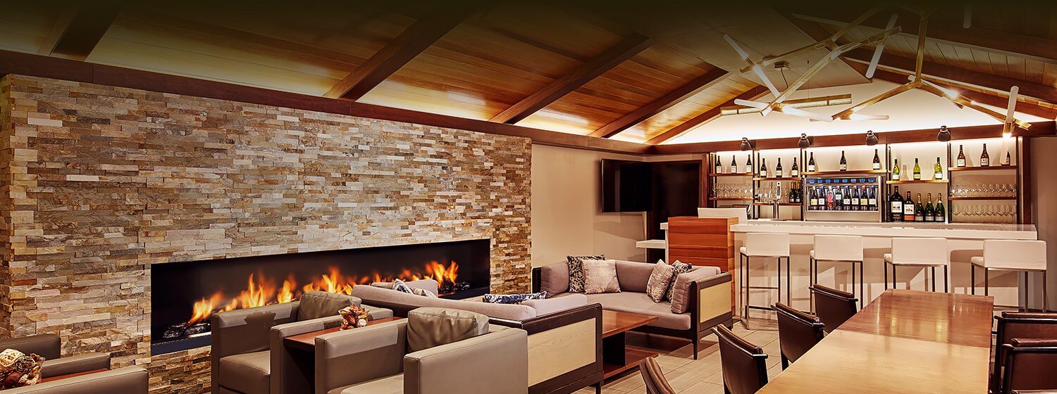 Interior of a lounge and bar seating area with wooden ceilings, couches and chairs around a stone fireplace and various wines displayed behind the bar counter
