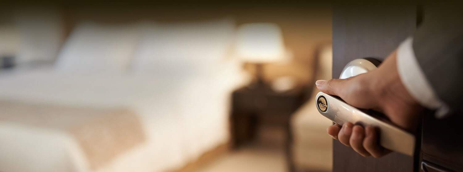 A hand opening the door to a guest bedroom with the interior of the room blurred