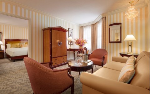 Grand Deluxe Suite with living area, two chairs, coffee table and sofa, bedroom in the back with king size bed