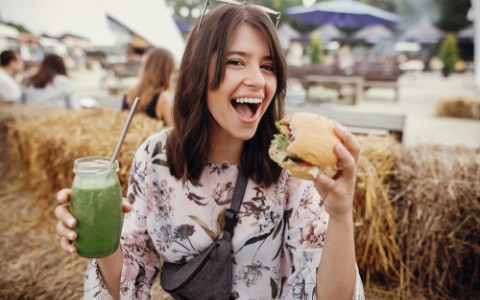 woman holding veggie burger and green juice