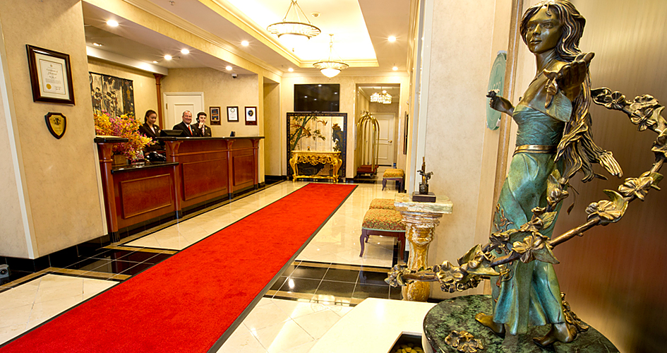 lobby of hotel with red carpet, marble floors and statue, reception desk to the left