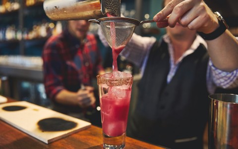 bartender straining pink drink into glass