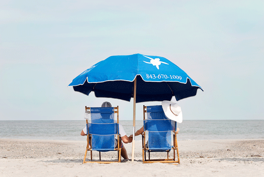 two people in beach chairs under an umbrella on beach