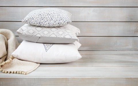Three stacked decorative pillows on wooden bench 