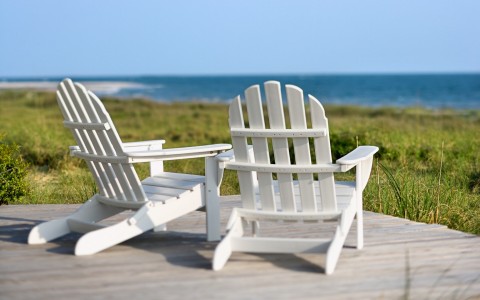 Close up of white wooden chairs overlooking grass field & ocean 