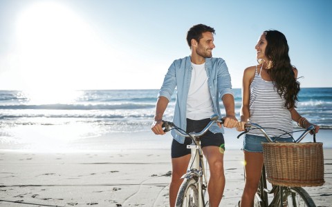 Couple standing with bikes on sand with ocean in the back