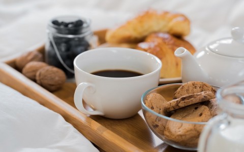 Wooden tray on bed with coffee, blueberries, cookies & croissants 