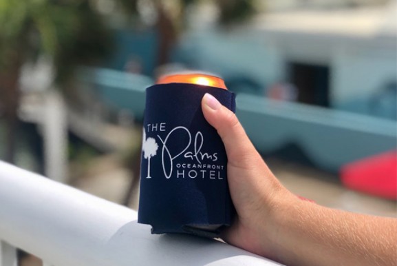 hand holding a beer with the hotel logo on a koozie